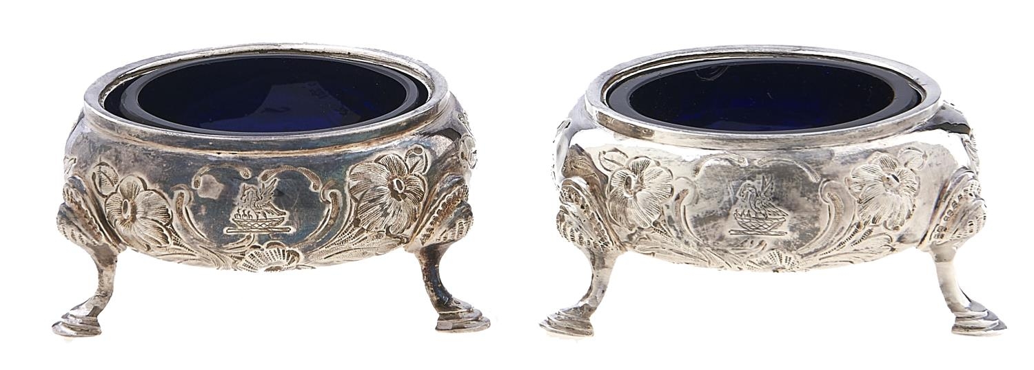 A pair of Victorian silver salt cellars, chased with roses, on three feet, crested, blue glass