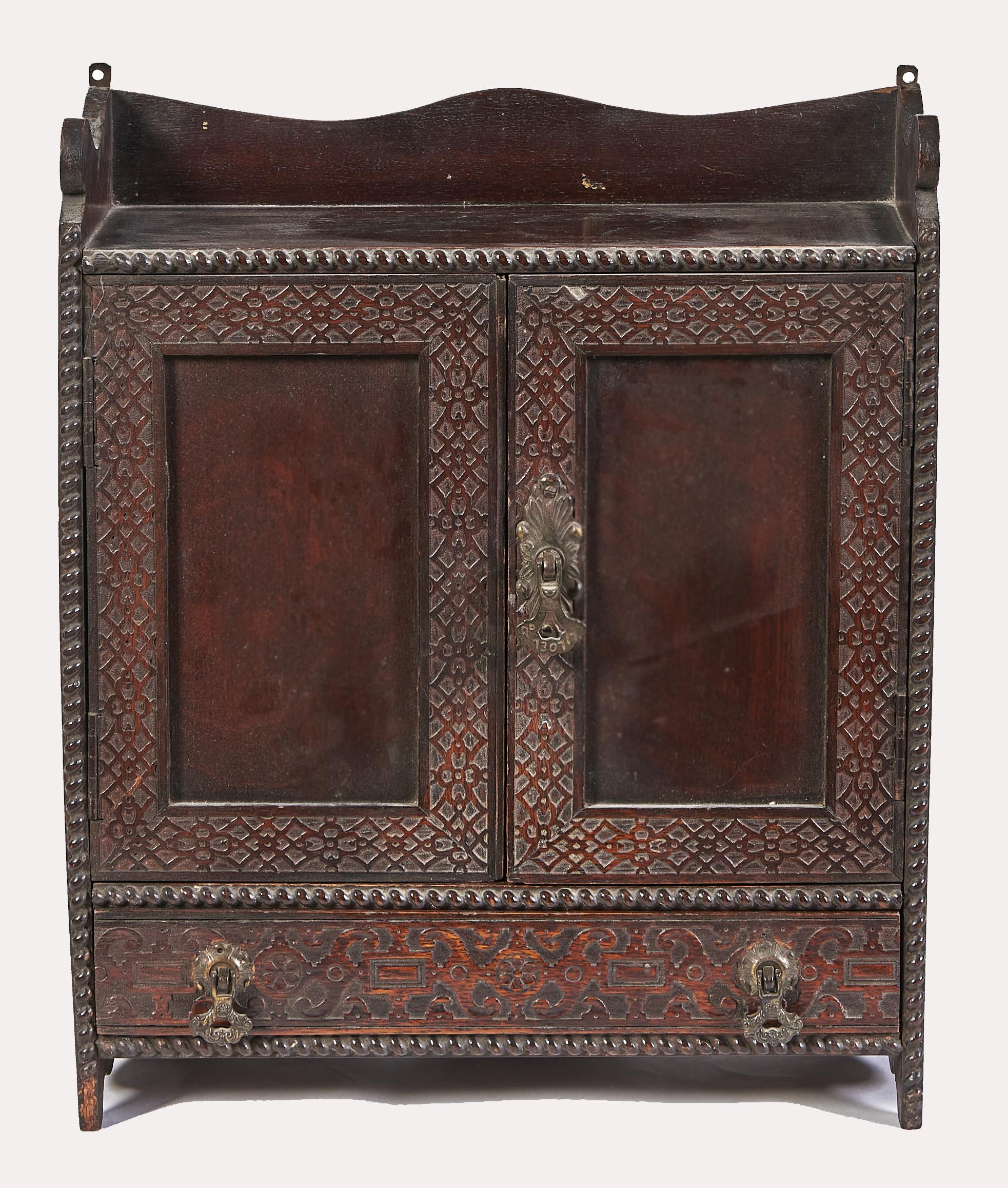 An Edwardian blind fret carved stained-oak hanging cupboard, with panelled doors and drawer, brass