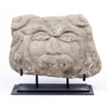 A stone fragment carved with a face, 26cm l, metal stand Condition evident from image