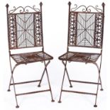 A pair of painted iron and wirework garden chairs, the ornate s-scroll top rails above spider's