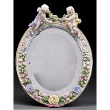 A German oval floral encrusted dressing mirror, early 20th c, crested by putti with flowers, 22.