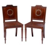 A pair of Regency brass mounted mahogany hall chairs, the panel back applied with a brass ring