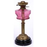 An Edwardian brass oil lamp, with cranberry glass fount and brass burner, on black glazed foot, 45cm