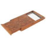 A finely carved wood travelling mirror, early 20th c, the sliding cover and back decorated with a