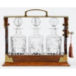 A brass and oak tantalus, early 20th c, with set of three cut glass cylinder decanters and stoppers,