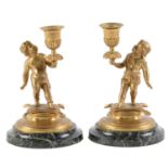 A pair of gilt bronze table candlesticks modelled as infants on cushions, late 19th c, on shallow