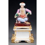 A Derby figure of a Turk, c1830, richly attired and seated cross legged on a cushion with gilt