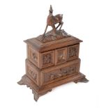 A Swiss carved walnut trinket box, c1900, in the form of a chest of drawers surmounted by a deer,