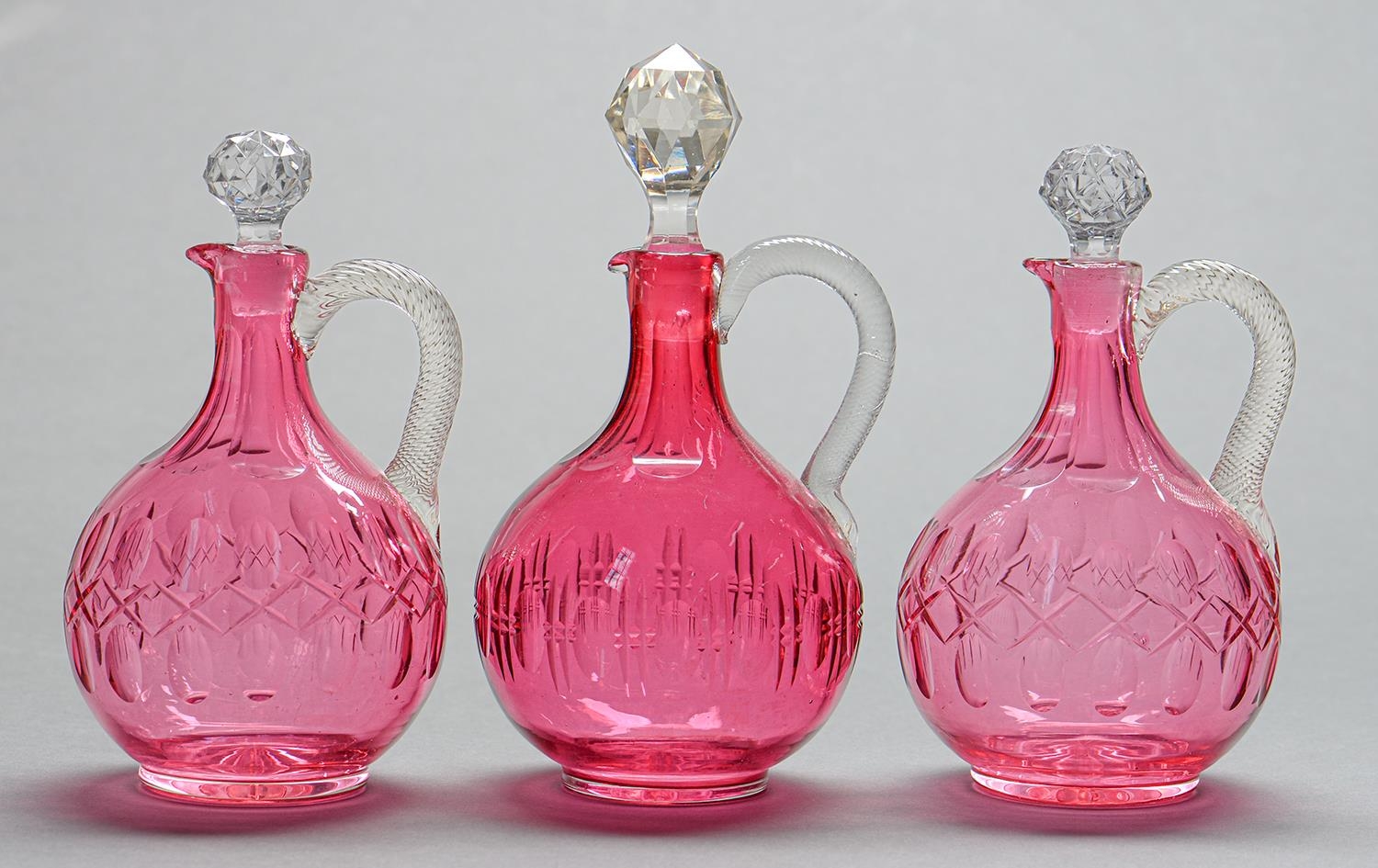 One and a pair of Victorian cranberry glass jugs, with clear snake handle and faceted stopper,