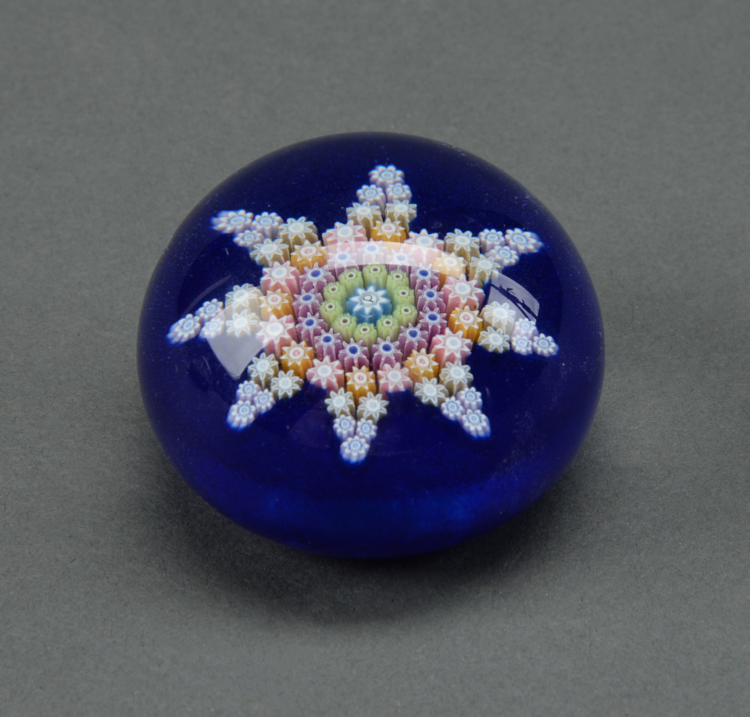 A glass millefiori paperweight, 20th c, of star form on a blue cushion, 62mm diam Good condition