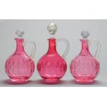 One and a pair of Victorian cranberry glass jugs, with clear snake handle and faceted stopper,