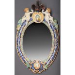 An Italian maiolica mirror, late 19th c, the oval frame surmounted by an eagle and two seated putti,