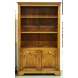 An oak open bookcase, with adjustable shelves, the lower part enclosed by a pair of raised and