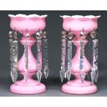 A pair of Victorian pink cased white glass lustres, with baluster stem and hung with prismatic cut