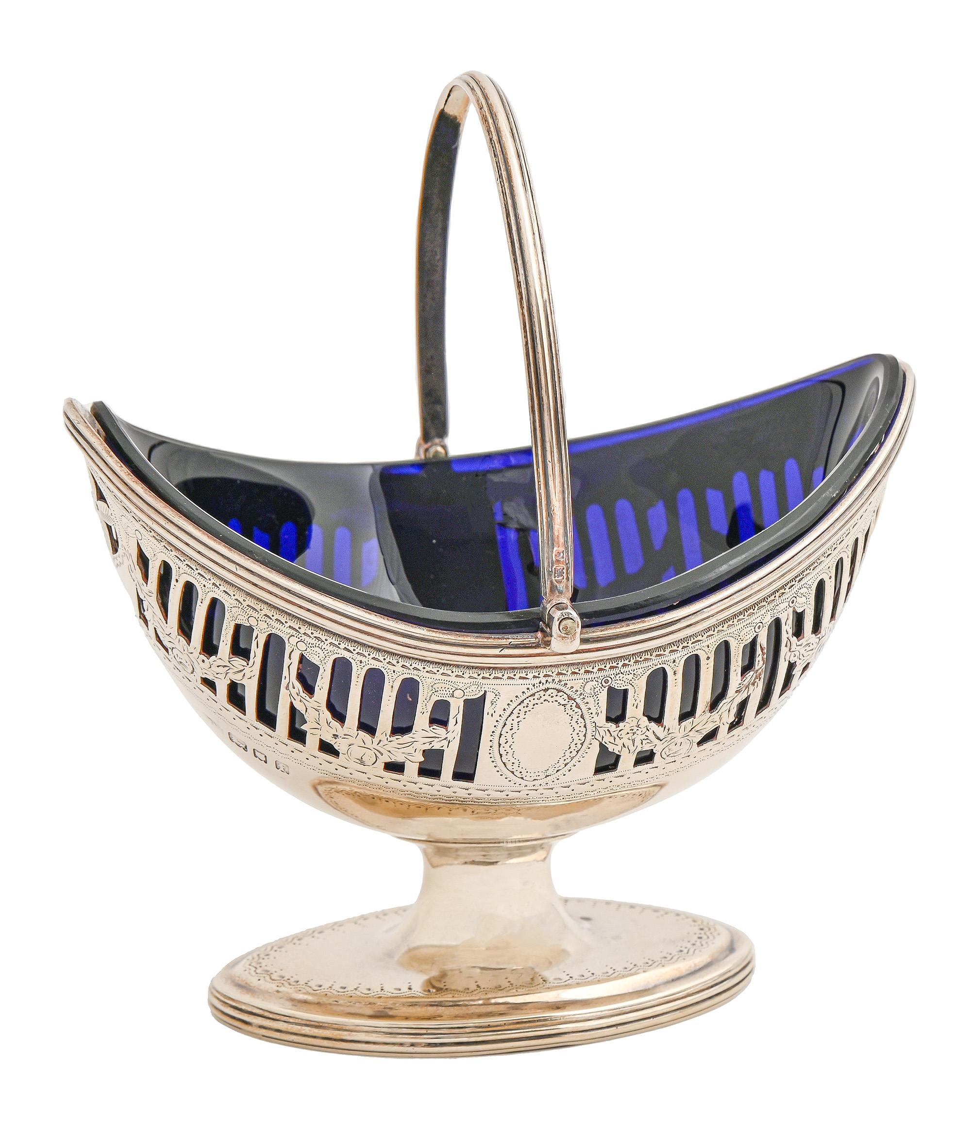 A George V pierced and engraved silver sugar basket, with reeded handle and rims, blue glass