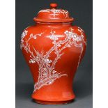 A Chinese red ground jar and cover, 20th c, decorated in white enamel with flowering prunus, 26cm