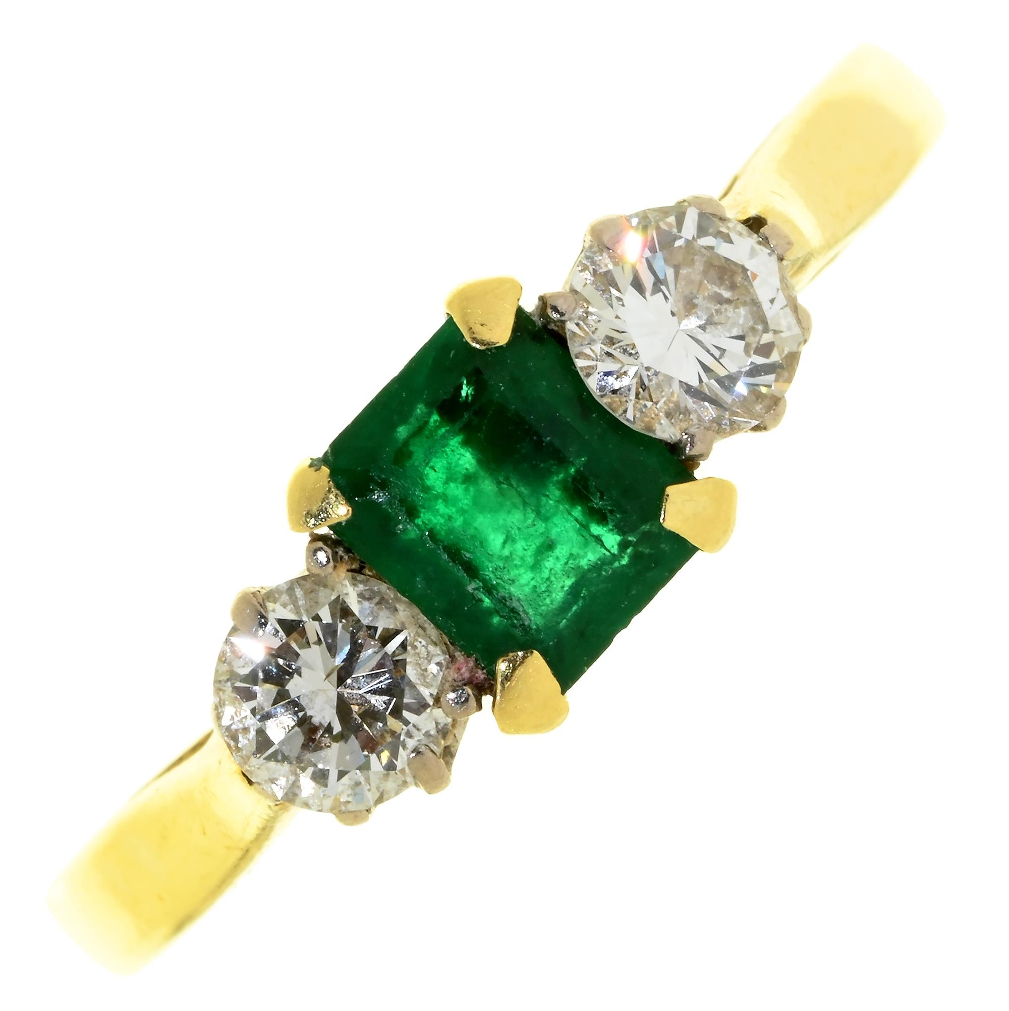 An emerald and diamond three stone ring, the step cut emerald flanked by evenly sized round