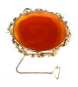 A late 19th century unmarked yellow metal brooch with oval set orange agate of oval form,