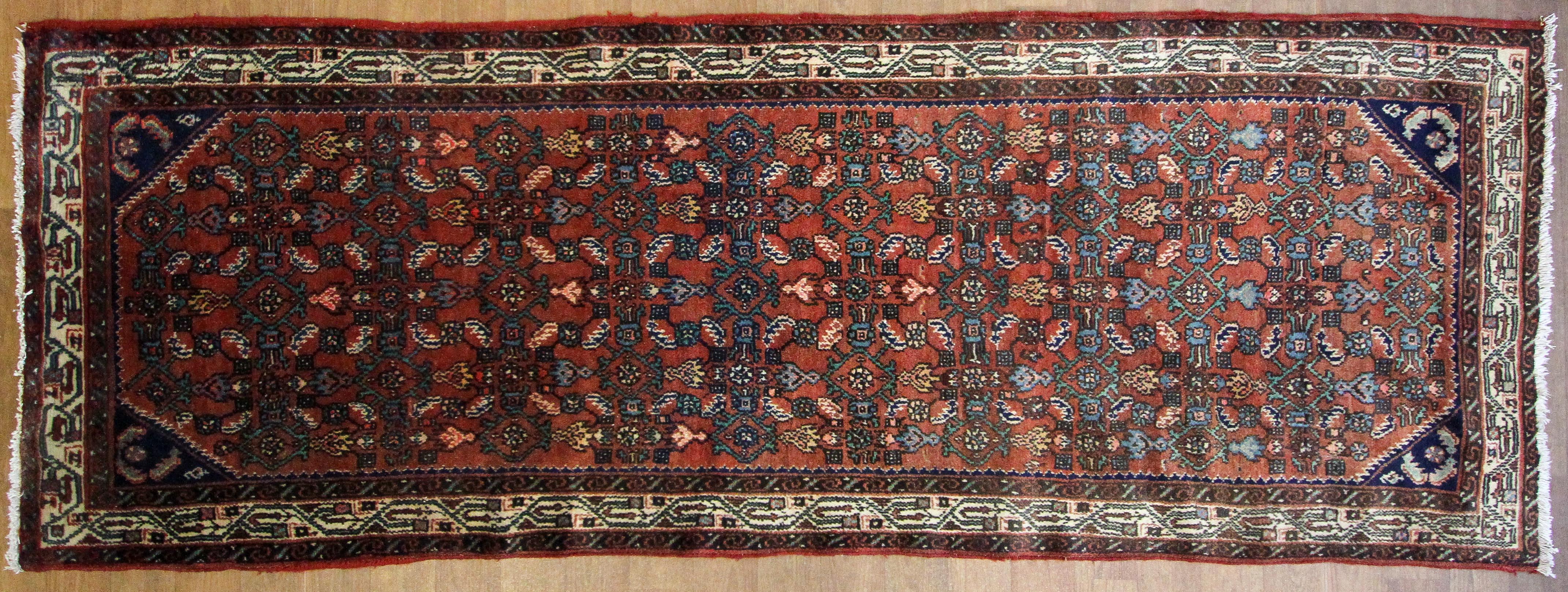 A Hamedan dark red ground rug, woven with a repeated geometric design in cream, blue and red.