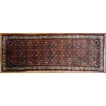 A Hamedan dark red ground rug, woven with a repeated geometric design in cream, blue and red.