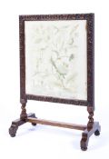 A late Victorian carved oak needlework fire screen,