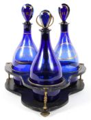 A set of three Regency Bristol blue glass spirit decanters in a papier-mache and brass stand,