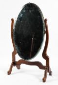 An early 20th century wooden swing mirror, the oval mirror itself with bevelled edge,