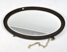 A bevelled edge wall mirror, of oval form, the mahogany frame with carved details,