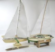 A wooden model of a yacht and one of a katamaran, both boats are decorated in cream and green,