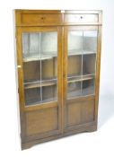 An oak glazed bookcase, a pair of short drawers positioned above the twin panelled doors,