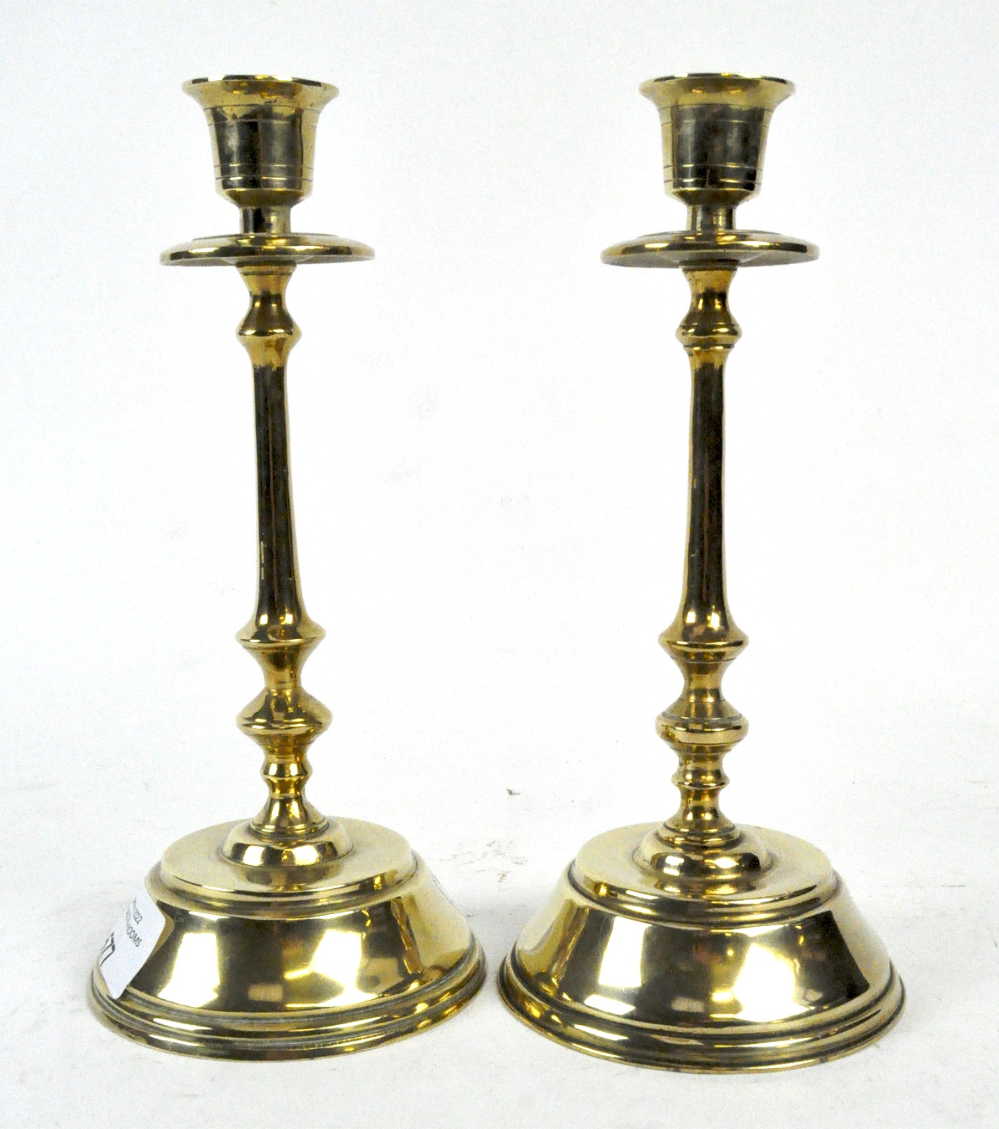 A pair of brass candle sticks, with thin stems and mounted on a circular base,