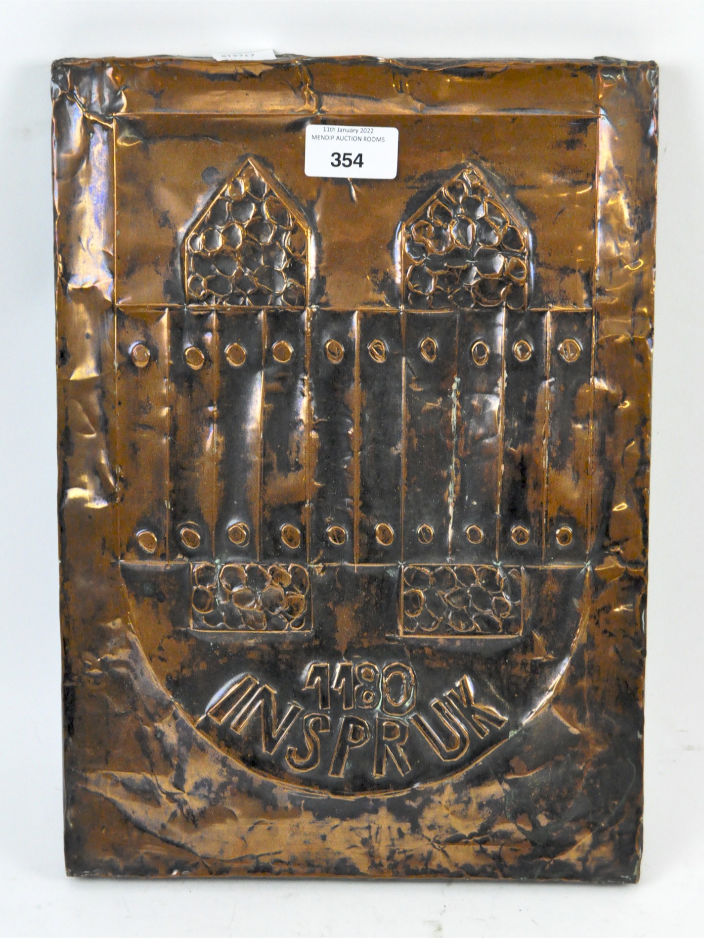 A hammered copper plaque, stating '1180 Inspruk' beneath a geometric design,