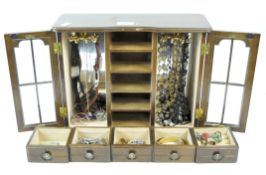 A vintage tabletop jewellery box cabinet containing a selection of costume jewellery,