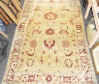 A large yellow ground rug with red and pink leaves and flowers within a cream ground border,