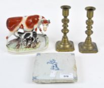A Staffordshire cow together with a Delft tile and pair of brass candlesticks,