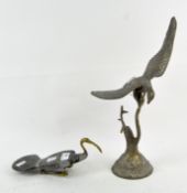 Two brass sculptures of birds, one perched on a tree, the other positioned on the ground,