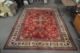 A large Oriental style woollen rug, the patterns on a red ground with cream borders.