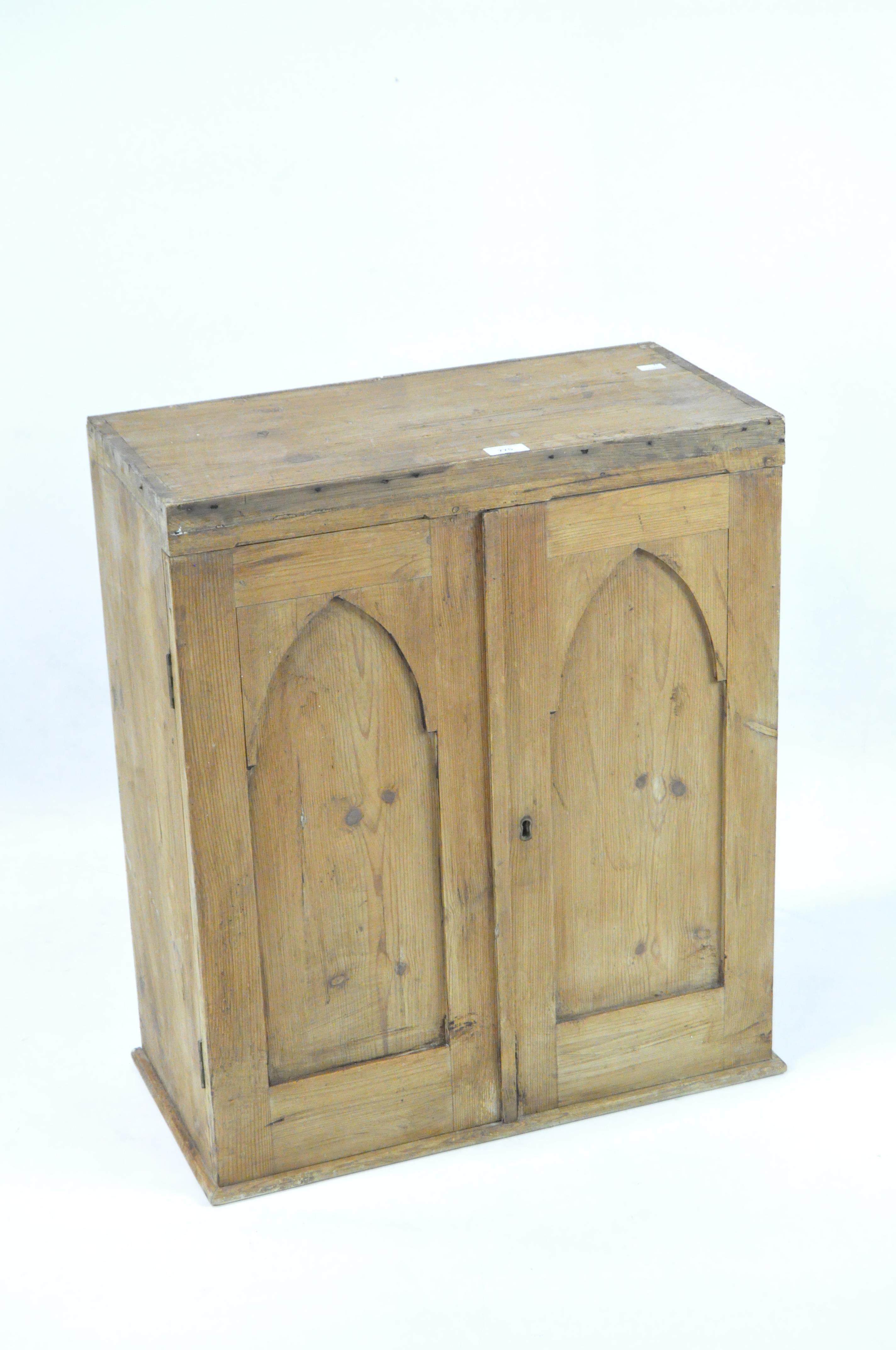 A small Victorian pine cupboard, featuring two shelves behind double doors with arched details,