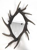 An oval wall mirror with a frame in the form of cojoined antlers,