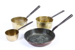 Three Victorian brass saucepans in various sizes and a frying pan, with iron handles,