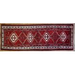 An Azari red-ground rug, woven with diamond shaped medallions in red and cream, 320 cm x 105 cm.