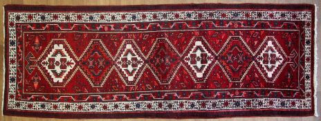 An Azari red-ground rug, woven with diamond shaped medallions in red and cream, 320 cm x 105 cm.