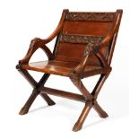 A late 19th century oak Glastonbury chair, carved with trefoil leaves to the panelled back,