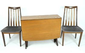 A wooden G-Plan drop leaf table and two chairs, the table with curved edges and a splayed support,