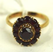 An 18ct gold ladies cluster ring, the large central red stone surrounded by ten smaller stones,