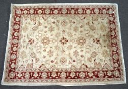 A woven Eastern rug, decorated with floral patterns on a beige ground, encircled by a red border,