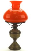 An early/mid 20th century brass oil lamp, adorned with an orange glass shade,