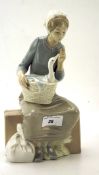 A Nao figure of a seated woman holding a basket containing a duck,