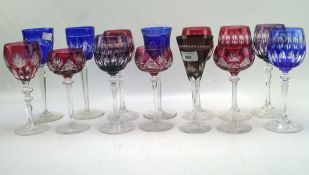 A collection of coloured glass, including multiple wine glasses in blue cranberry and purple,