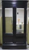 A large black lacquered wardrobe with glazed double doors, with moulded top and base, dismantled,